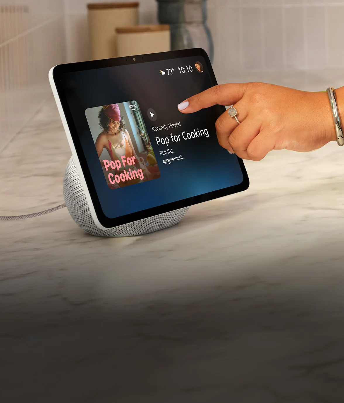 Un dedo toca la pantalla del Echo Show 11 para poner música.
