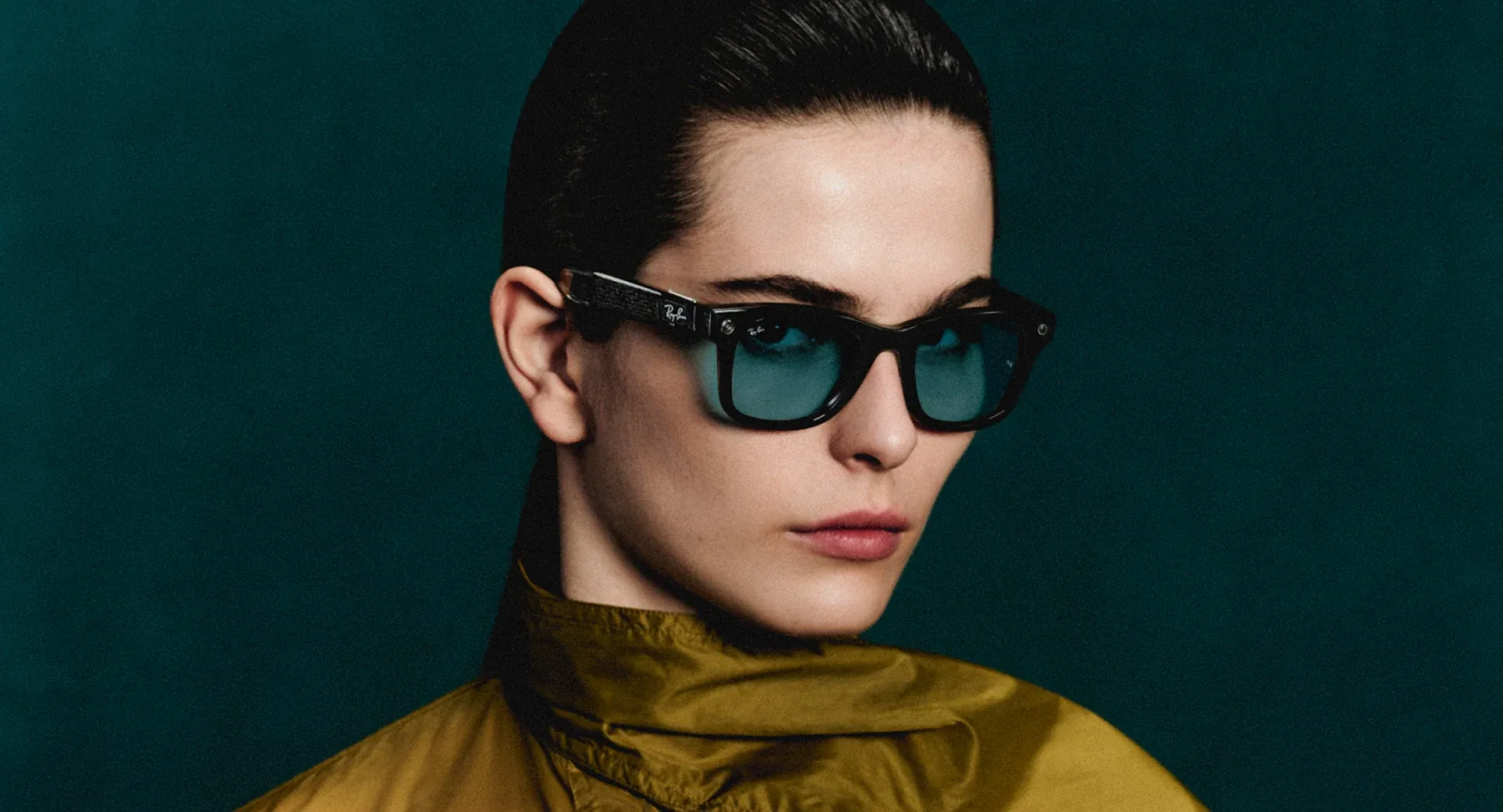 Una mujer con las Ray-Ban Meta Wayfarer negro transparente de lentes aguamarina, sobre un fondo verde petróleo.