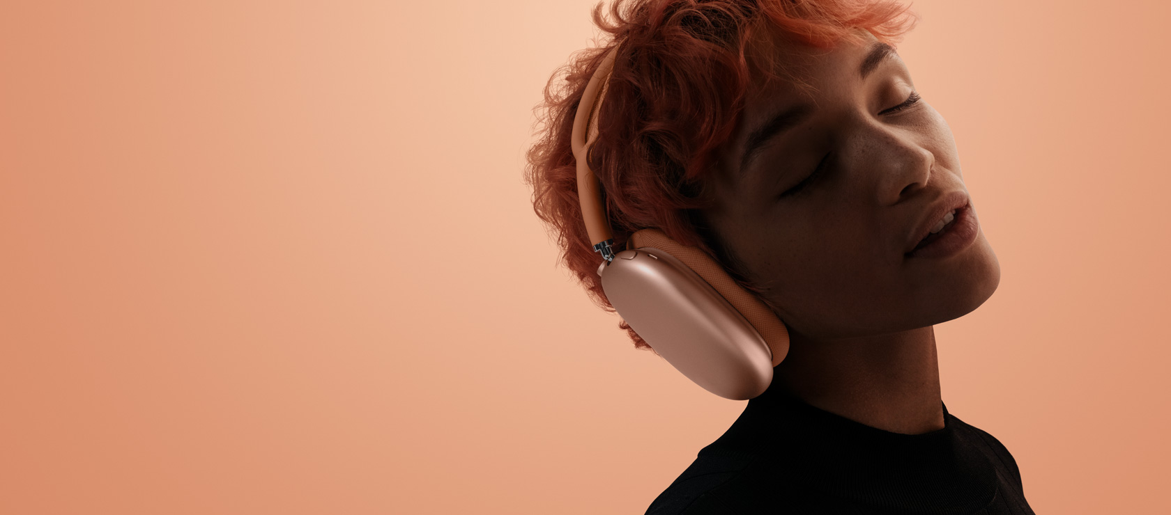 Una persona con la cabeza inclinada y los ojos cerrados con unos AirPods Max  2 puestos, color naranja, sobre un fondo naranja y rosa