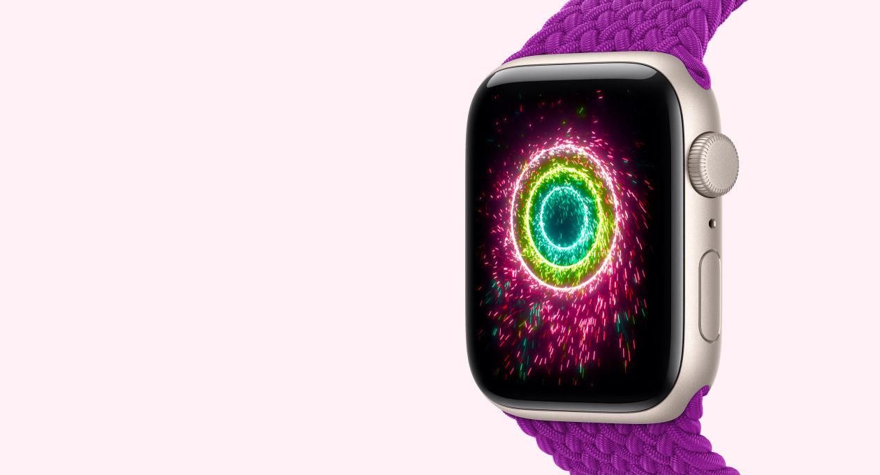 Apple Watch SE 3, caja de aluminio, blanco estelar, la pantalla muestra los círculos de Actividad con el estilo de fuegos artificiales, parte lateral derecha, Digital Crown, micrófono, botón lateral, correa uniloop trenzada, magenta