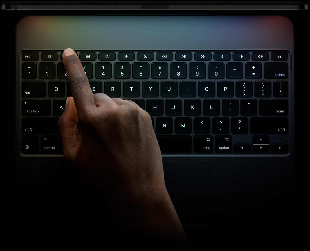 Un iPad Pro, posición horizontal, color negro espacial, perfil superior, conectado a un Magic Keyboard, parte frontal, posición horizontal, teclas negras retroiluminadas, fila de teclas de función exclusivas, Esc, Tabulador, Bloq Mayús, Mayús, Control, Opción, Mayús, Eliminar, Retorno, teclas de flecha en forma de T invertida, trackpad integrado
