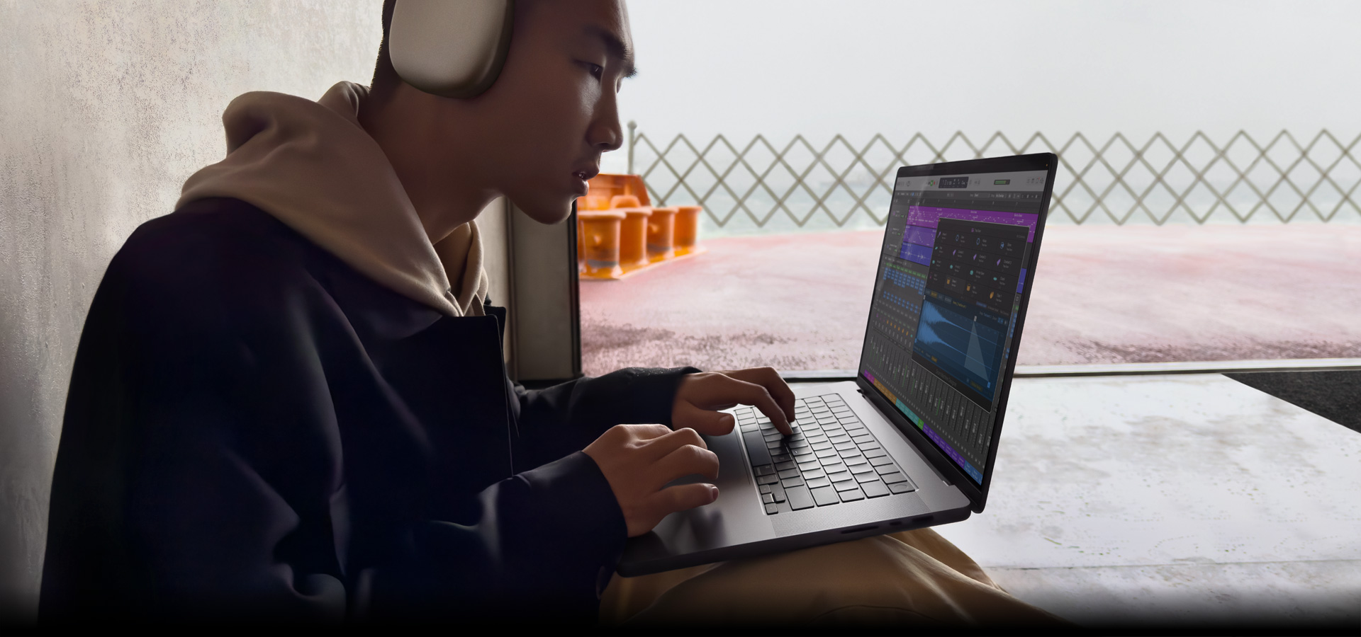 Vista lateral de una persona con unos AirPods Max que está usando Logic Pro en una MacBook Pro de 16 pulgadas, la pantalla muestra el espacio de trabajo de Logic Pro