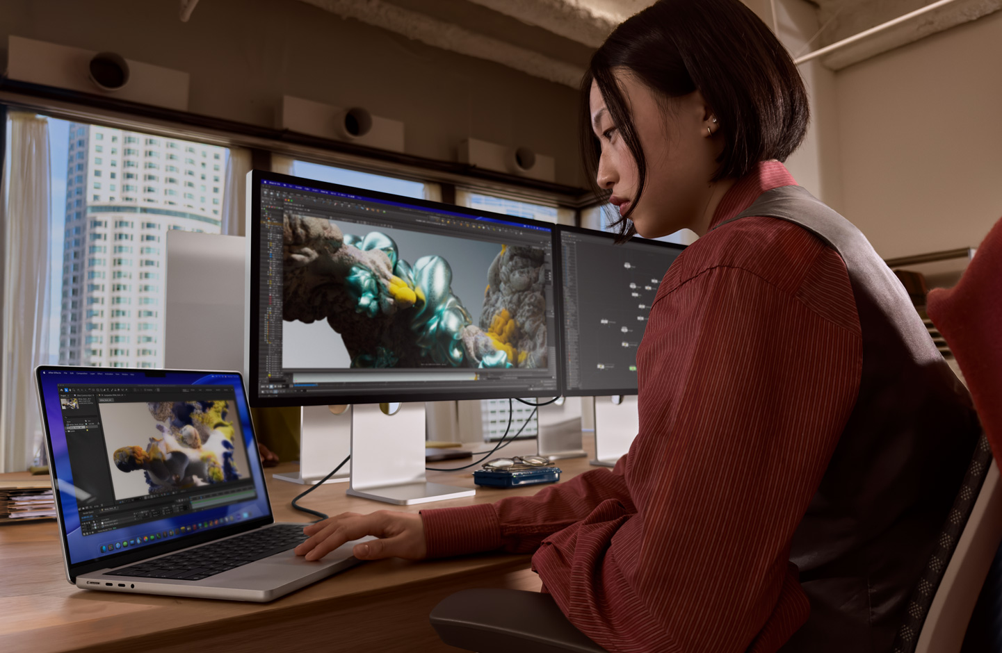 Una persona en una oficina trabaja en un portátil MacBook conectada a un monitor Studio Display XDR mediante un puerto Thunderbolt 5