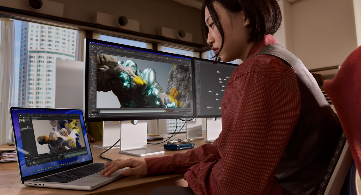 Una persona en una oficina trabaja en un portátil MacBook conectada a un monitor Studio Display XDR mediante un puerto Thunderbolt 5