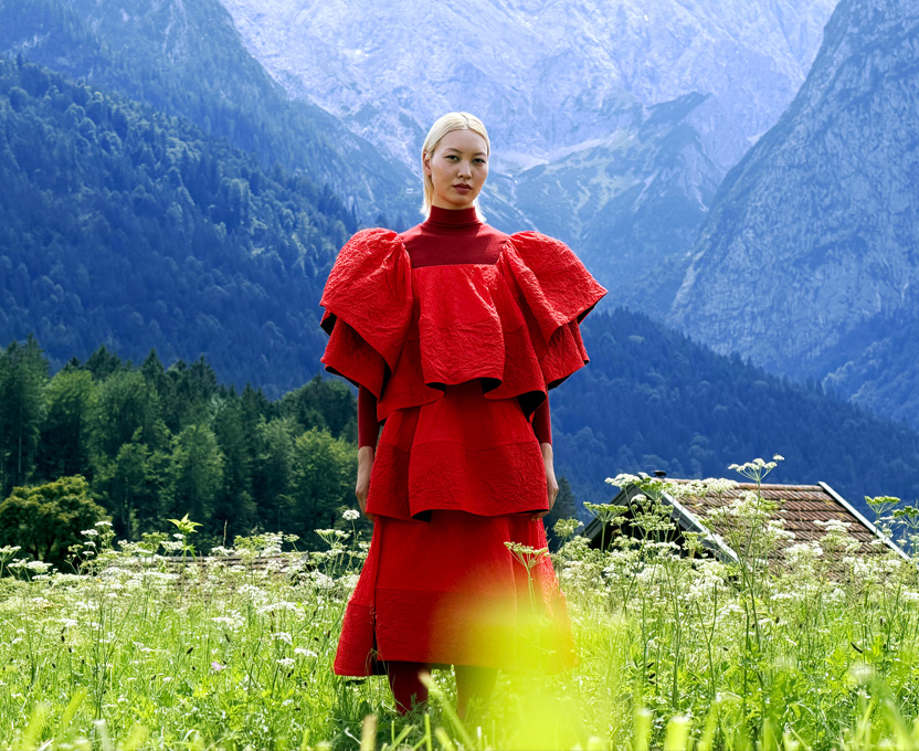 Una modelo con un vestido rojo intenso en un valle de montaña, se muestra la amplia gama de colores del monitor Studio Display XDR
