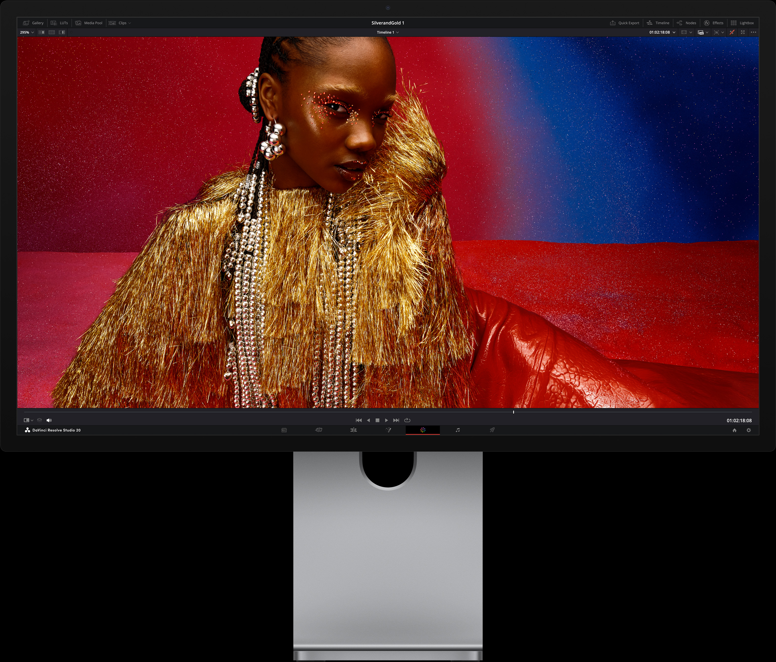 Una persona con un vestido rojo intenso y accesorios metálicos extragrandes sentada frente a un fondo con un degradado de azul y rojo, que destaca la calidad de imagen del monitor Studio Display XDR