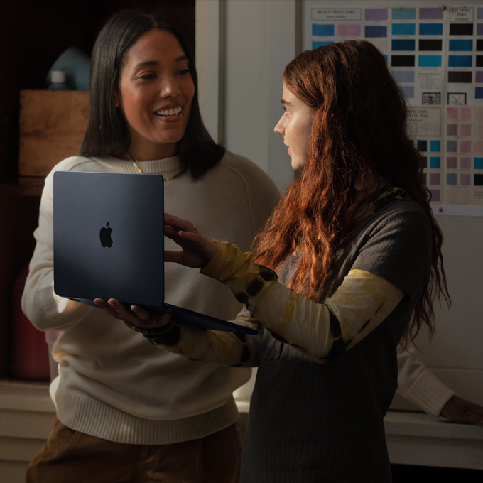 Una maestra y una estudiante conversan mientras sostienen un portátil MacBook
